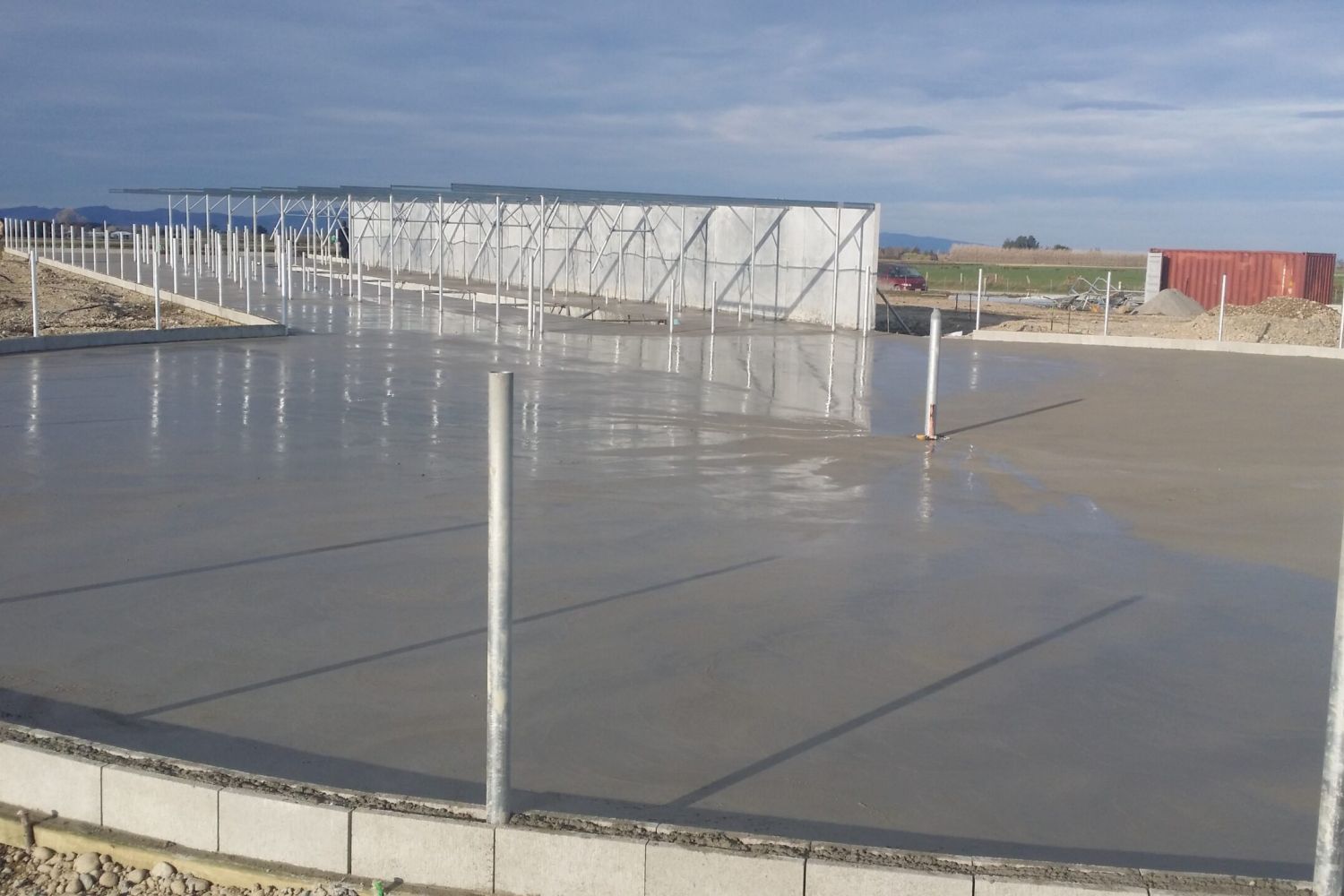 Concrete pour in progress inside a timber-framed dairy shed under construction, Ashburton